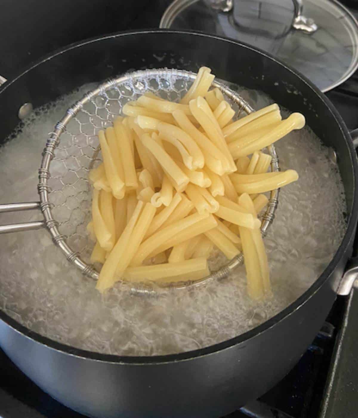 Colander holding pasta above boiling water.