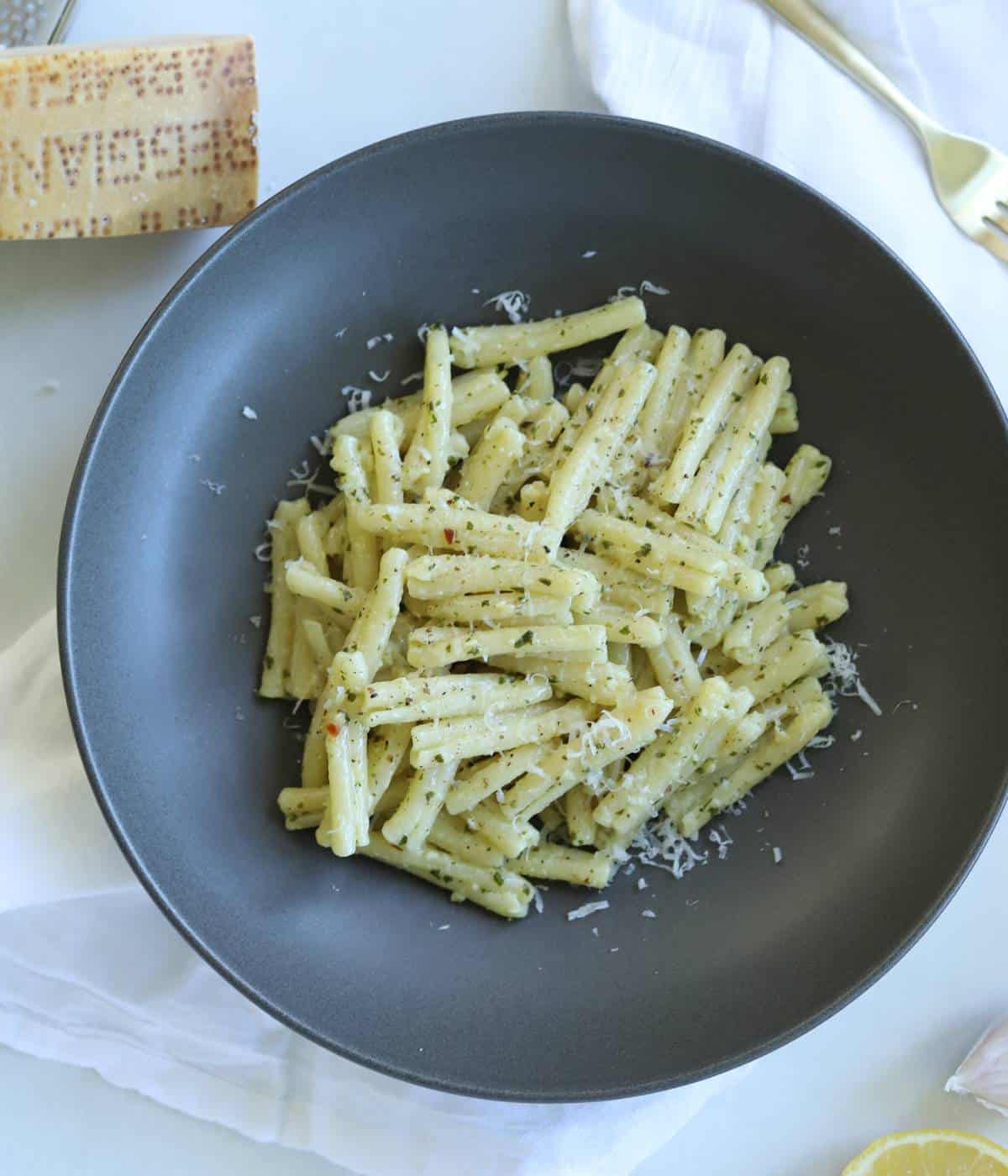 Pesto pasta in gray bowl topped with parmesan cheese.