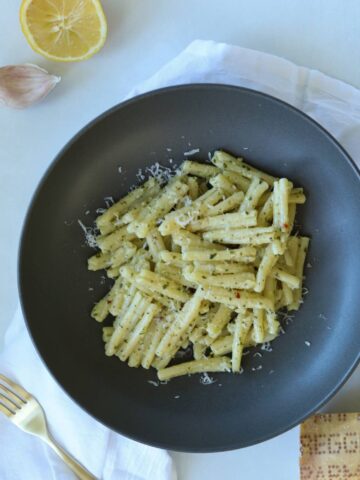 Pesto pasta in bowl with lemon and garlic on side.