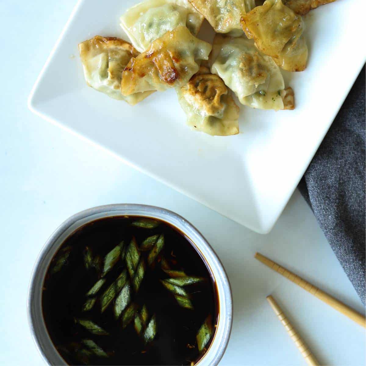 Gyoza sauce in bowl with wontons on platter.