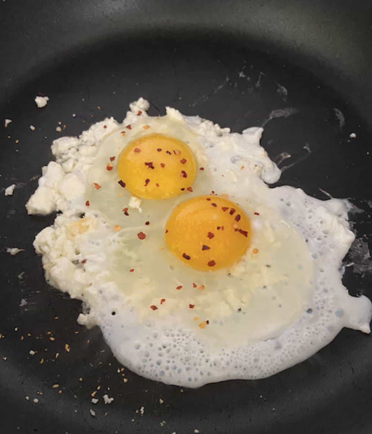 Fried eggs in pan topped with salt and red pepper flakes.