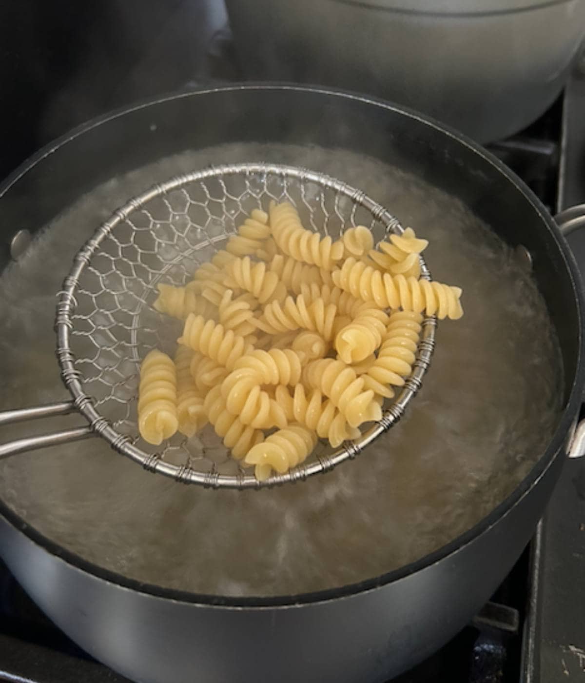 Colander with pasta over boiling water. 