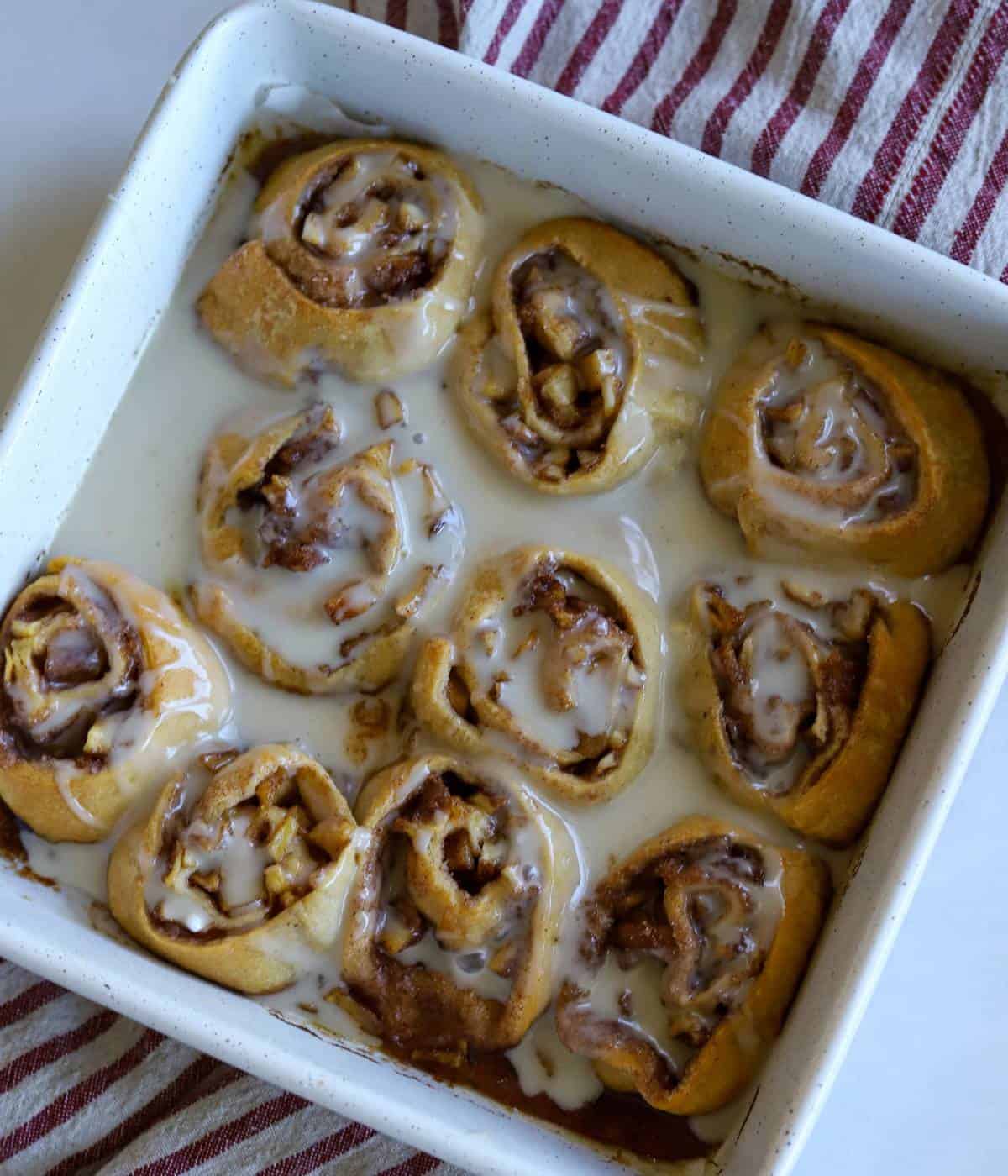 Apple pie cinnamon rolls with icing in pan.