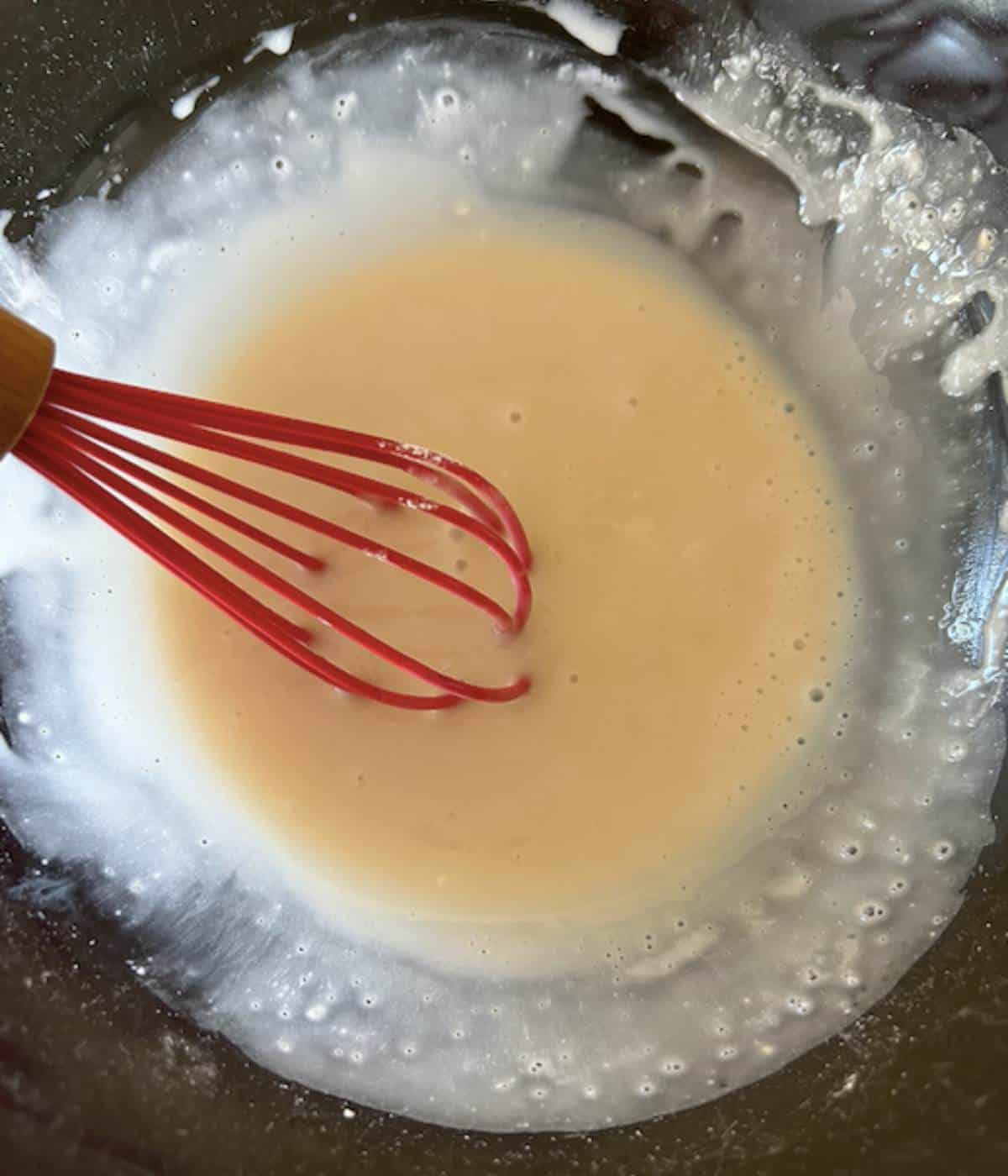 Cinnamon roll icing in glass bowl with whisk.