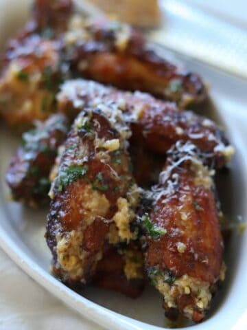 Chicken wings in white dish topped with garlic parmesan sauce.