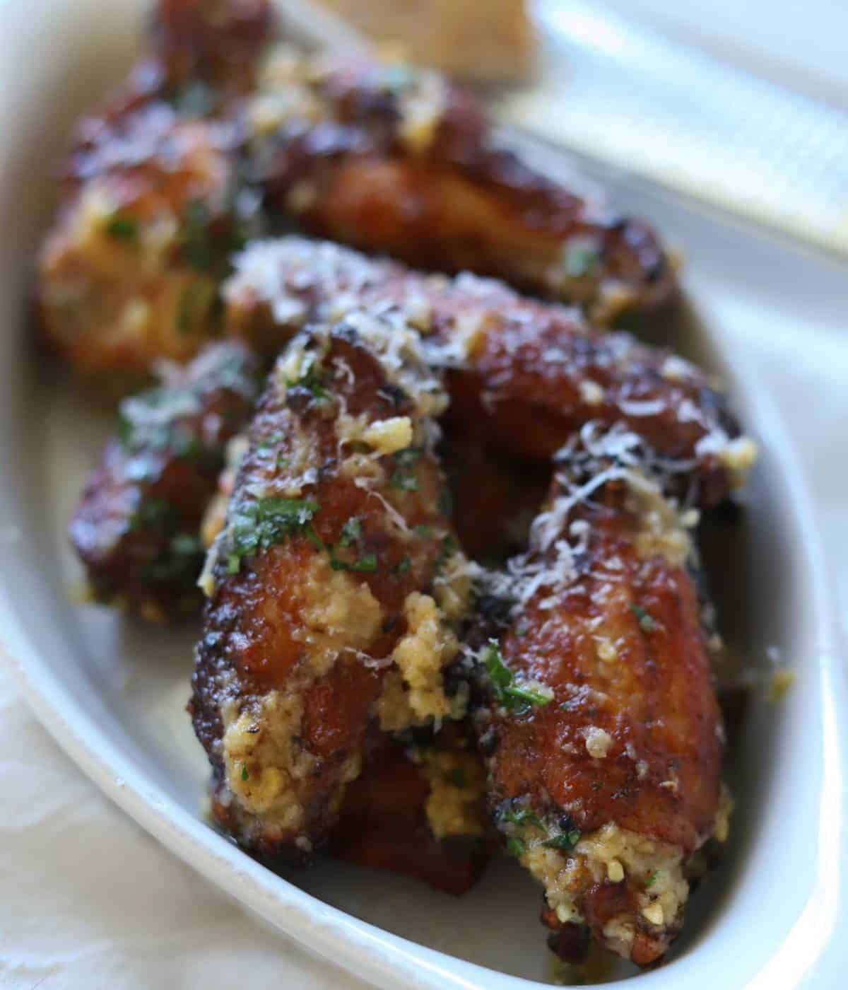 Chicken wings in white dish topped with garlic parmesan sauce.