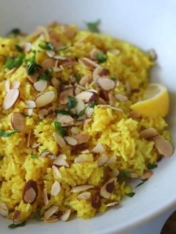 Mediterranean rice in white bowl with lemon wedges.