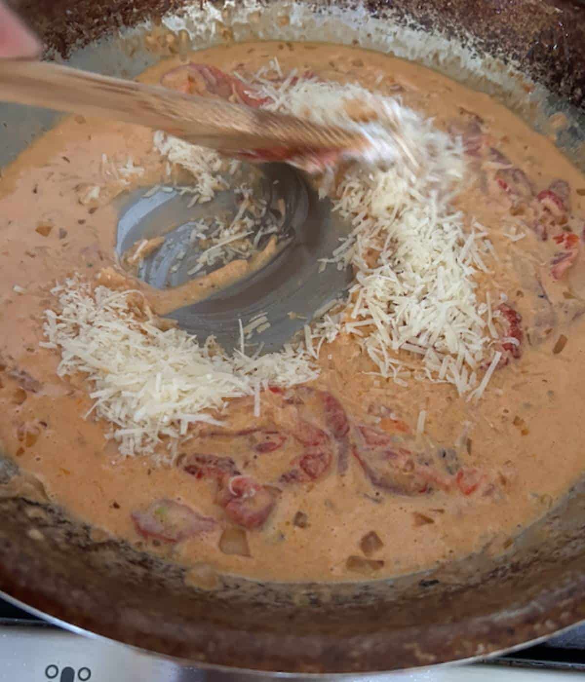 Creamy cajun sauce with wooden spoon stirring in cheese.