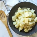 Stewed potatoes in gray bowl with wooden spoon.