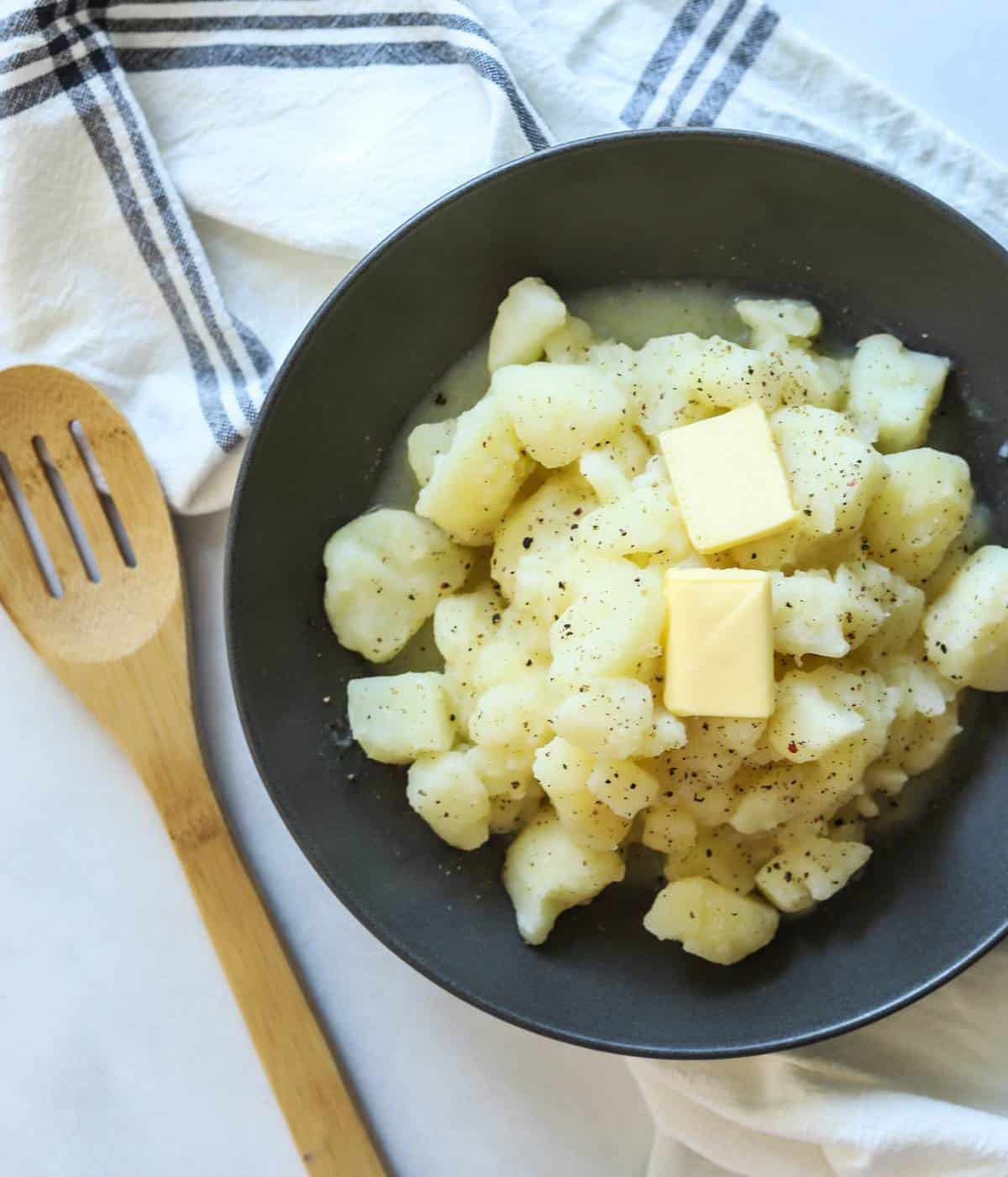 Stewed potatoes in gray bowl with wooden spoon.