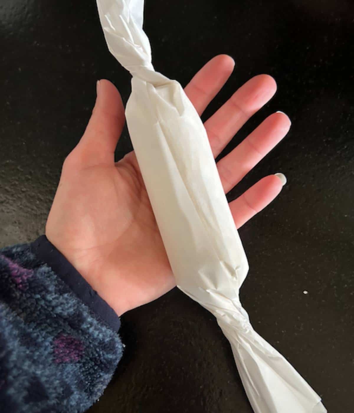 Hand holding garlic rosemary butter twisted inside parchment paper.