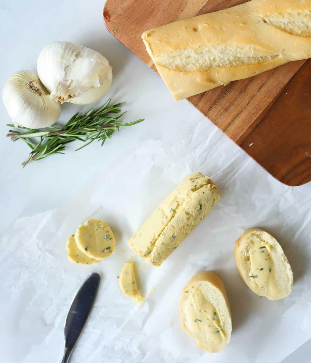 Compound butter on parchment paper with rosemary and garlic and bread.