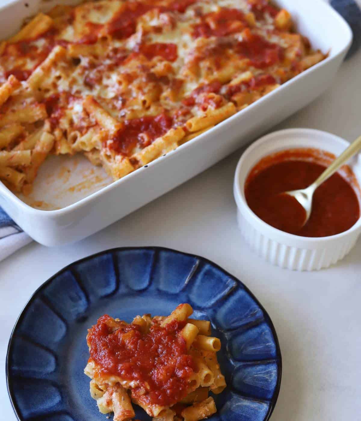 Casserole dish full of baked ziti with plate in front. 