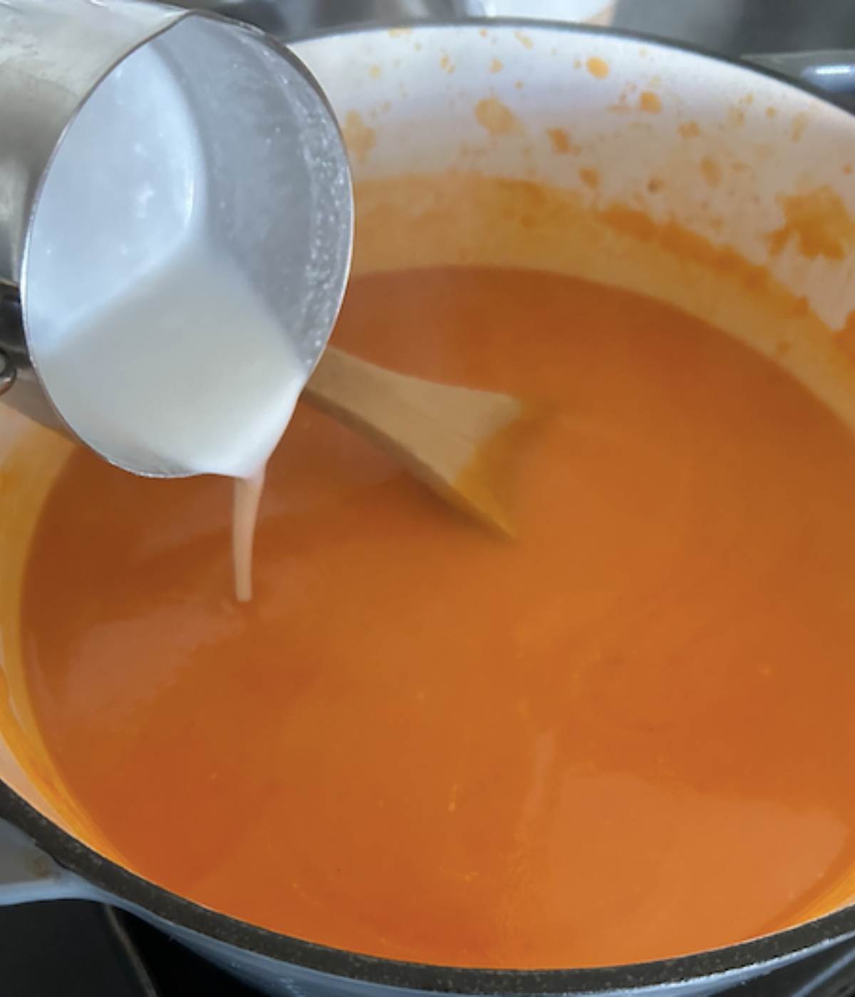 Coconut milk pouring into soup in dutch oven.