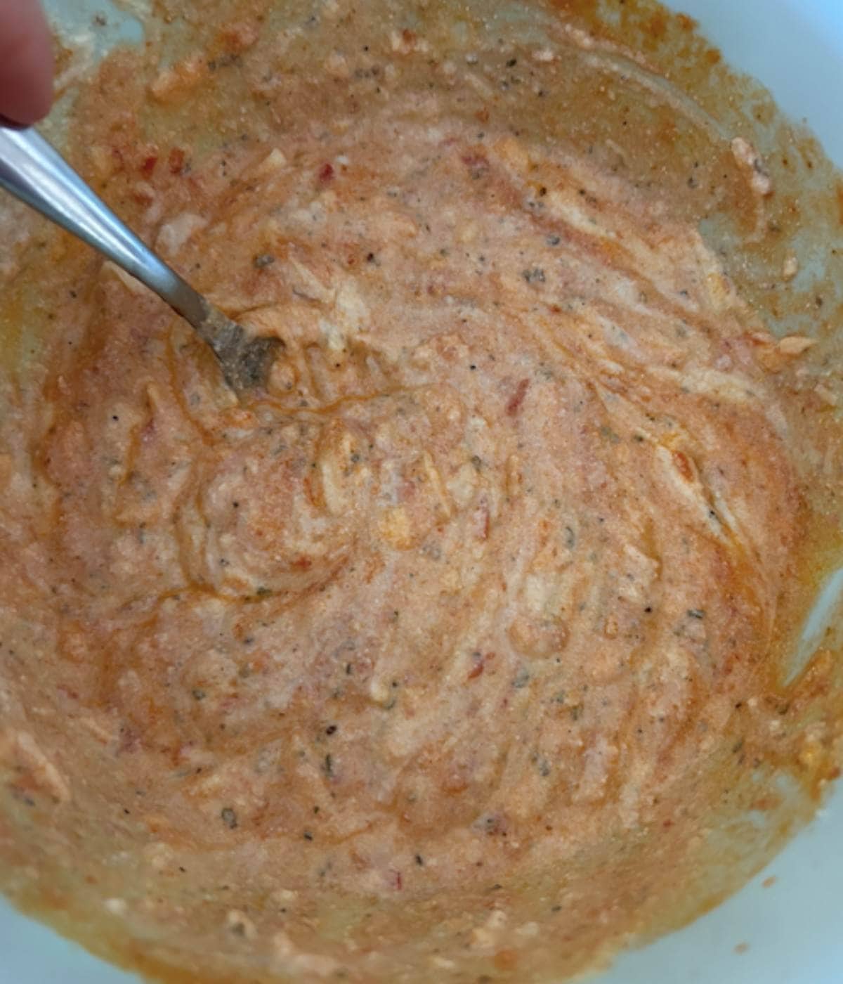 Saucy cheesy filling for ziti in blue bowl with spoon.