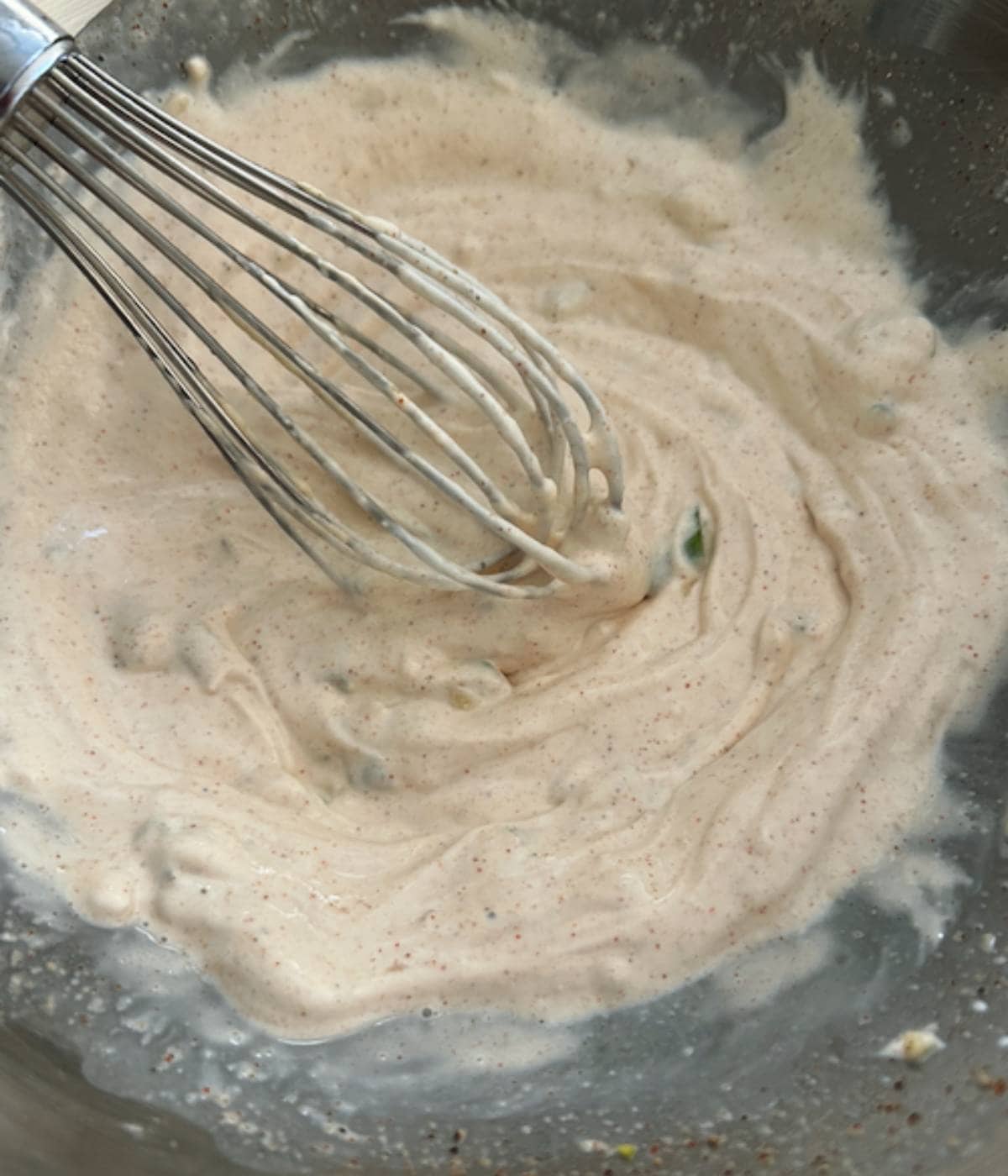 Whisking sour cream sauce in silver bowl.