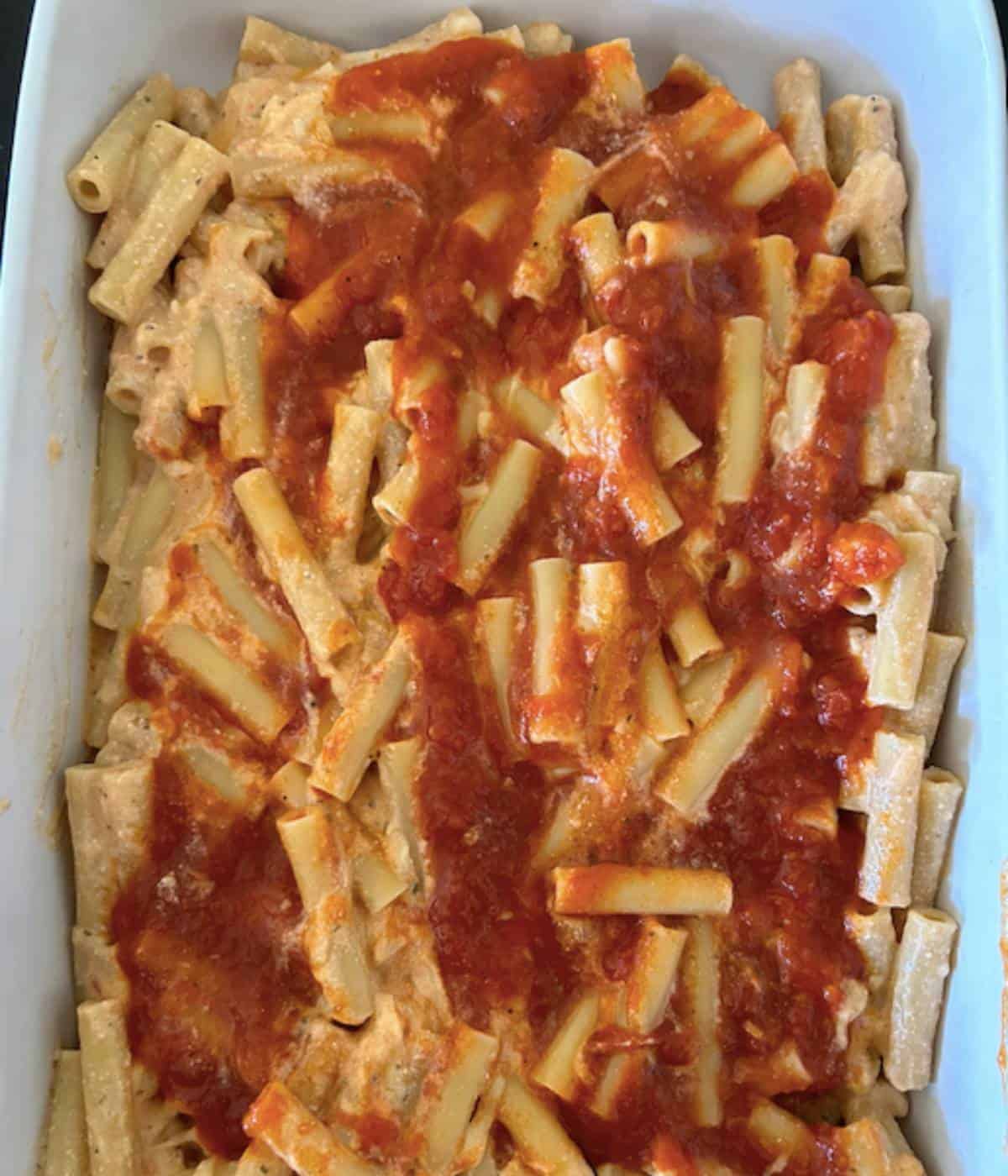 Baked ziti in casserole dish topped with sauce.