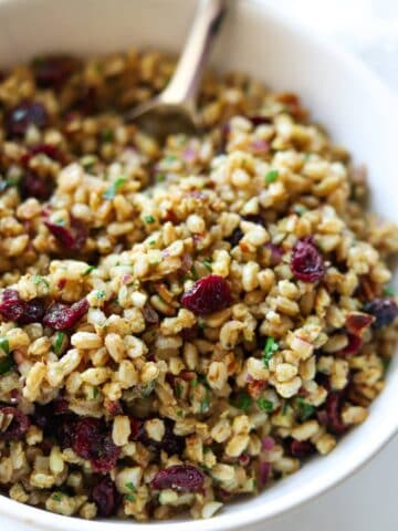 Farro salad in white bowl topped with pecans and cranberries.