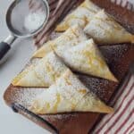 Six apple turnovers on platter with powdered sugar and caramel.