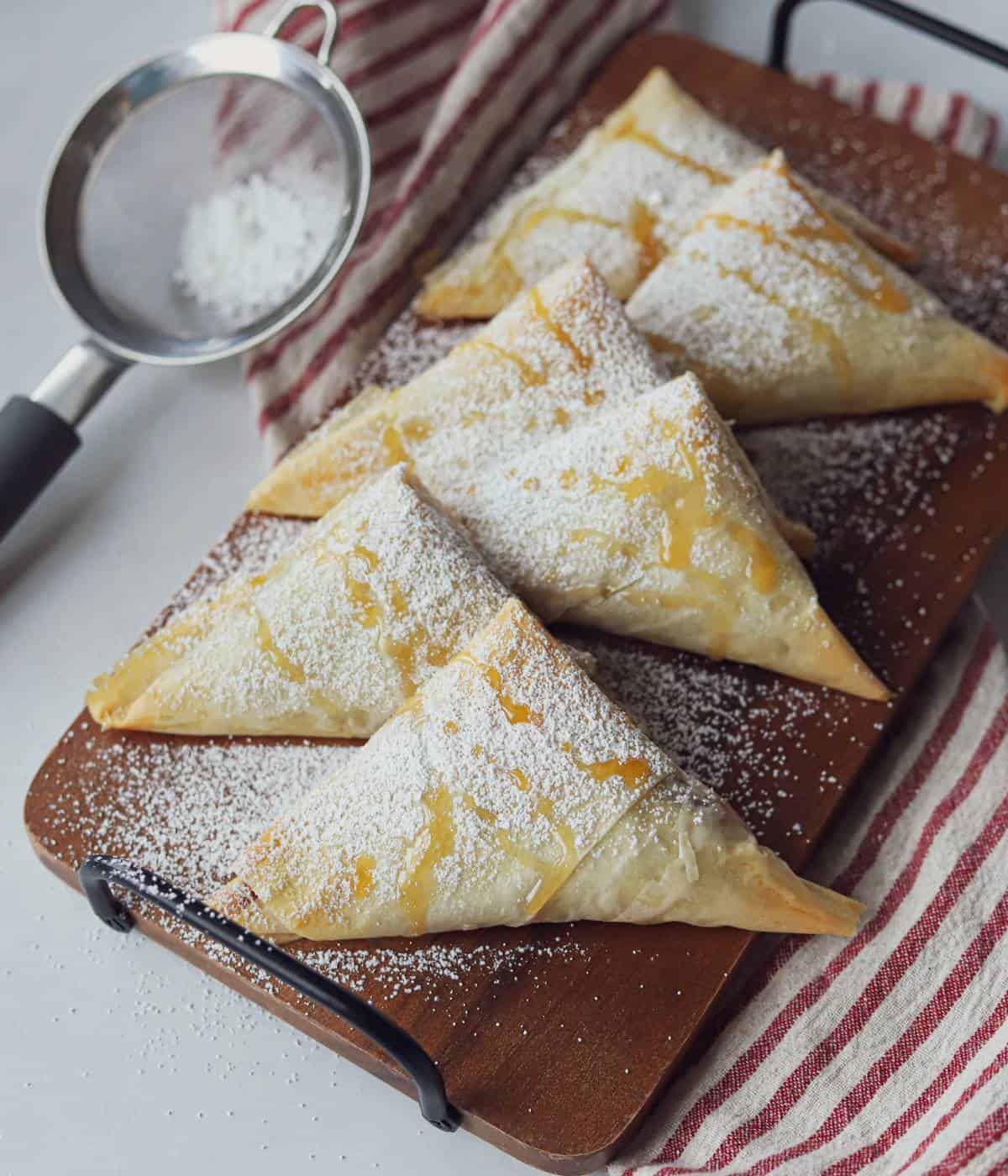 Six apple turnovers on platter with powdered sugar and caramel.