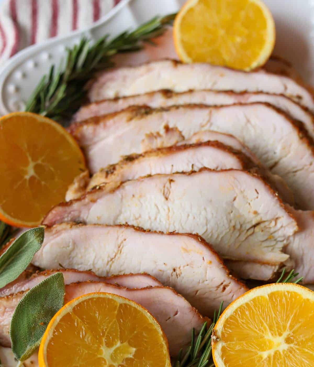 Smoked Turkey Breast on platter with fresh herbs and oranges.