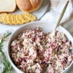 Turkey salad with cranberry sauce in bowl with breads and crackers behind it.
