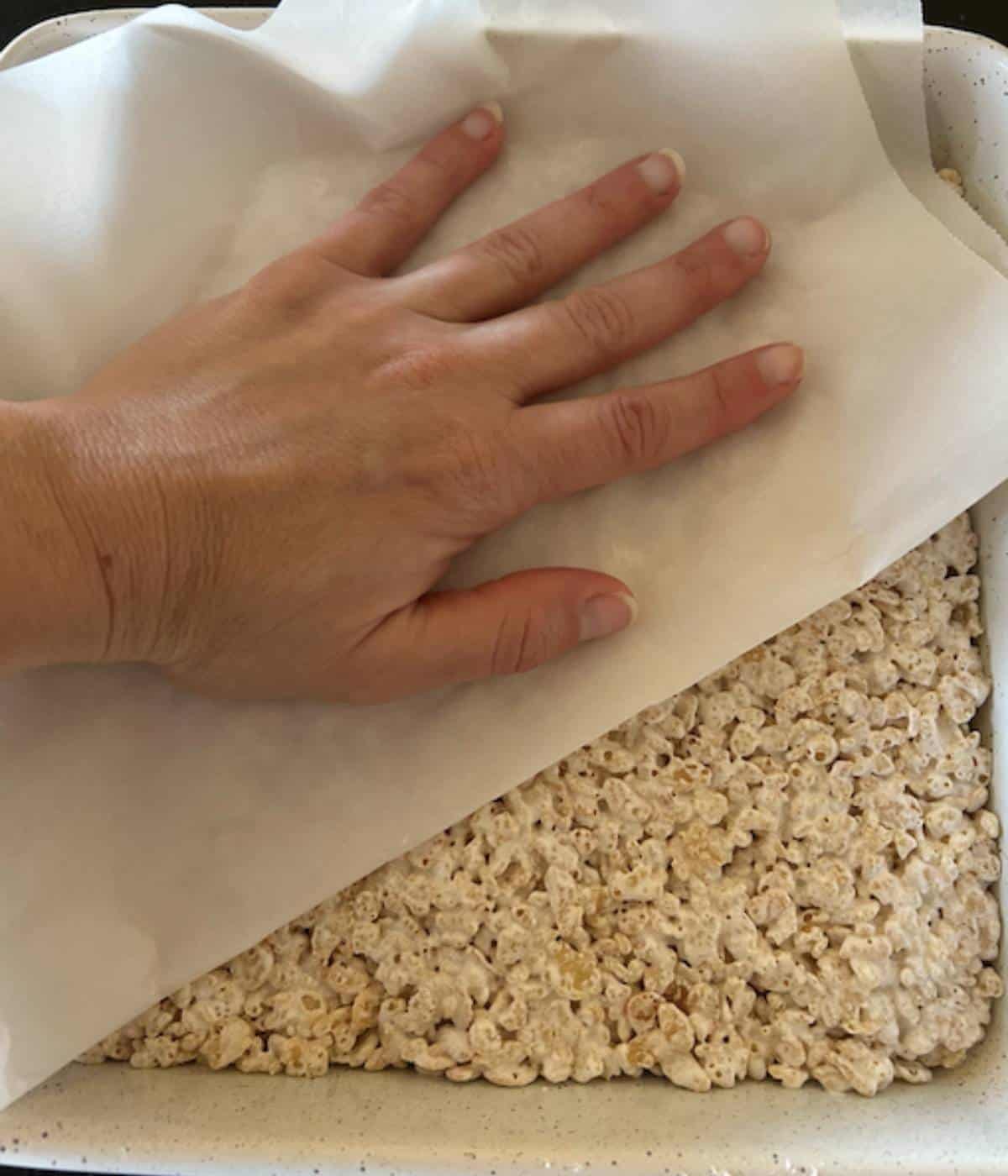 Hand pressing onto parchment paper to flatten rice krispie treats.