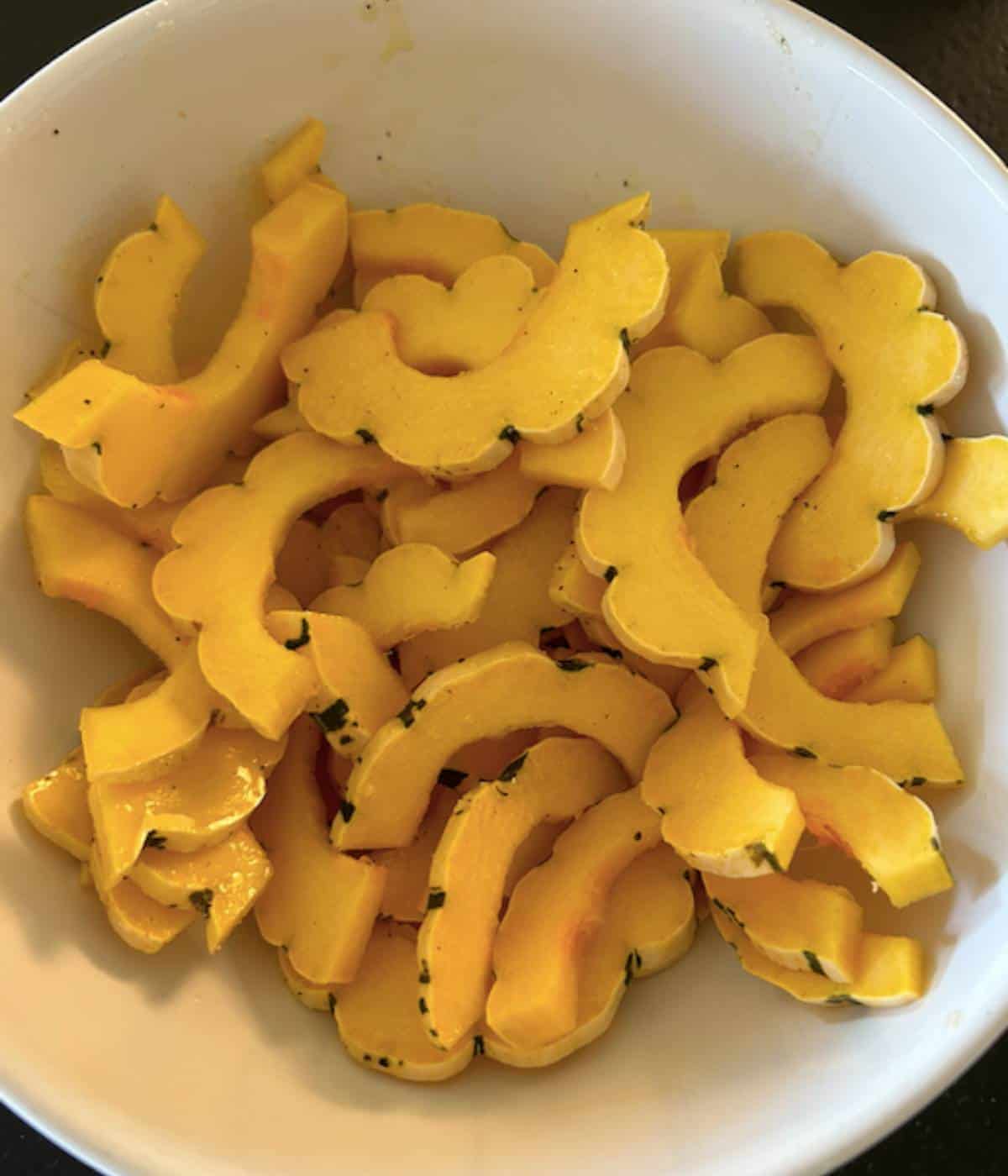 Squash tossed in olive oil and salt and pepper in white bowl.