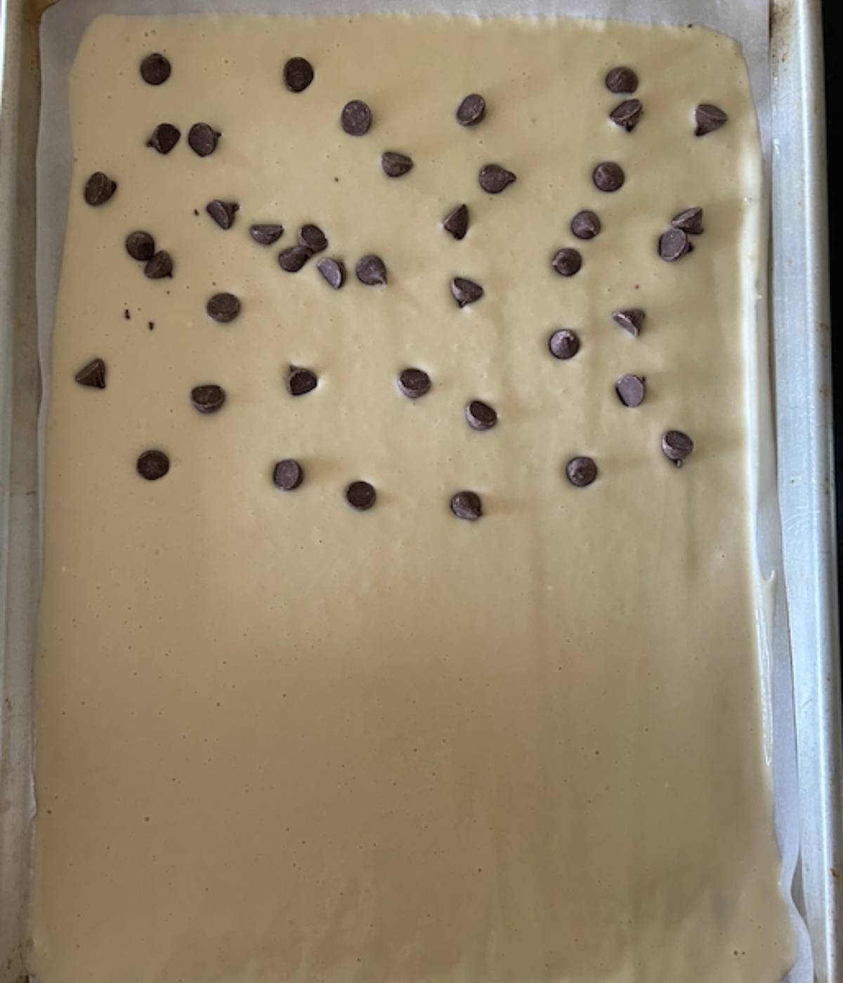 Pancake batter in sheet pan, half topped with chocolate chips.