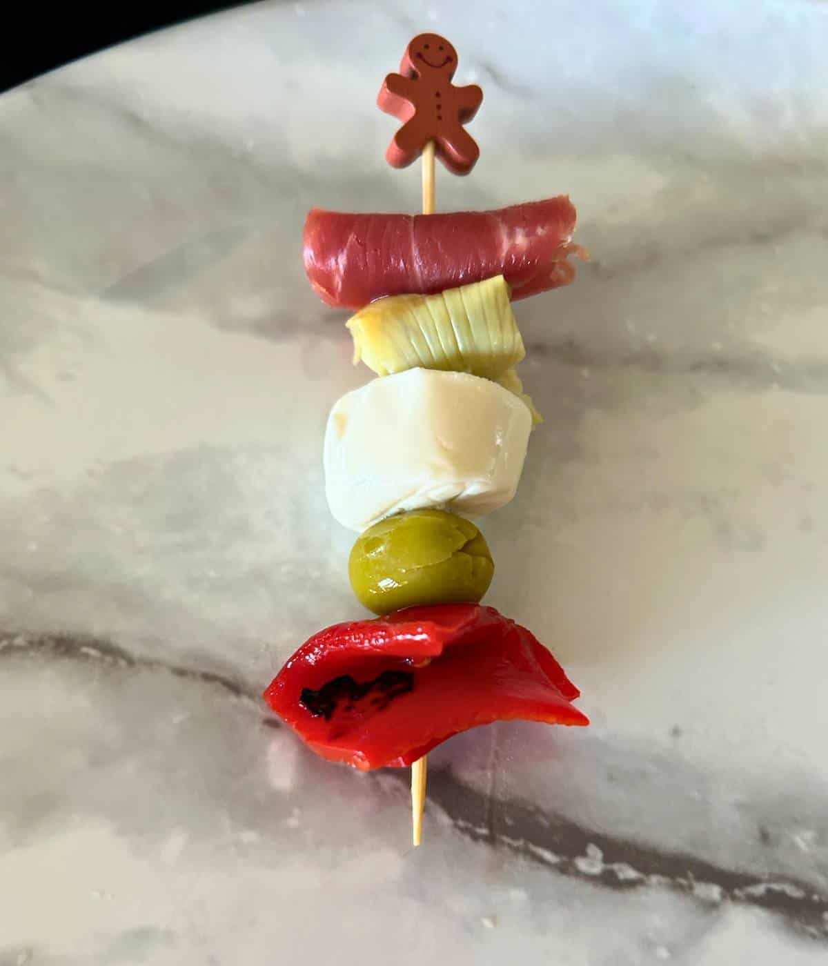 Charcuterie skewer with red peppers, olive, mozzarella, artichoke and prosciutto on stick.