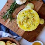 Baked brie topped with garlic butter and honey on serving dish.