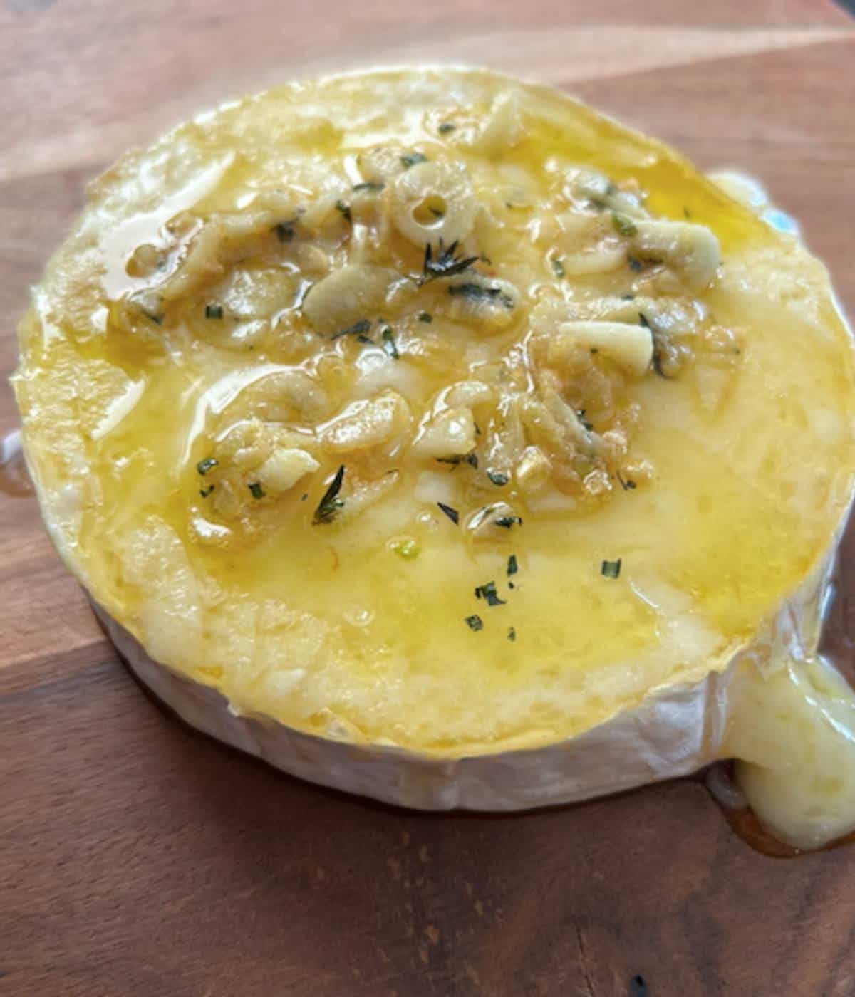 Garlic and herb topped baked brie on cutting board.