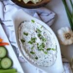 Green onion dip in white dish with vegetables and chips on the side.