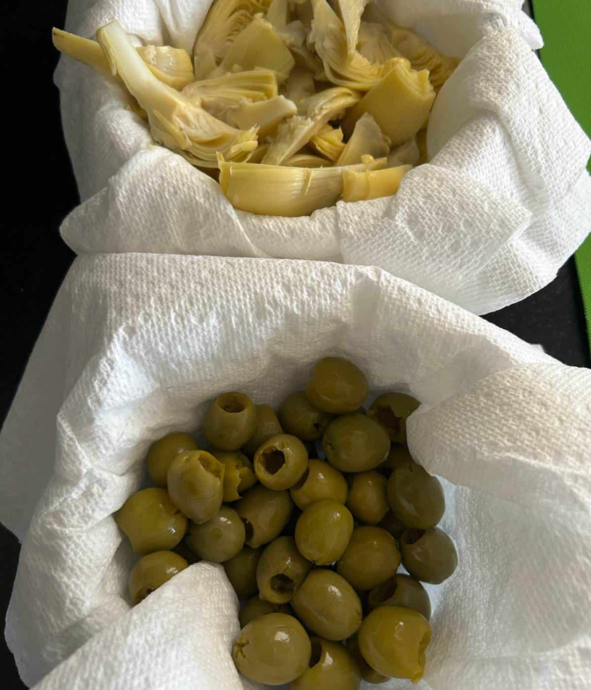 Olives and artichokes in bowls with paper towels to remove excess juices.