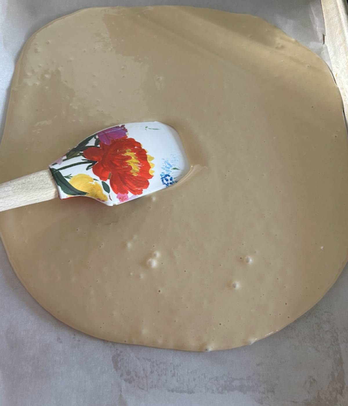 Spatula spreading bisquick pancake mix in cookie sheet.