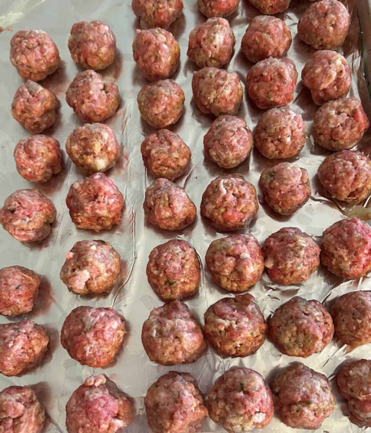 Mini meatballs rolled into balls on cookie sheet.