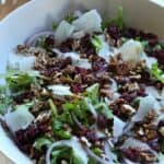 Spinach arugula salad topped with pecans, cranberries, parmesan cheese in large bowl.