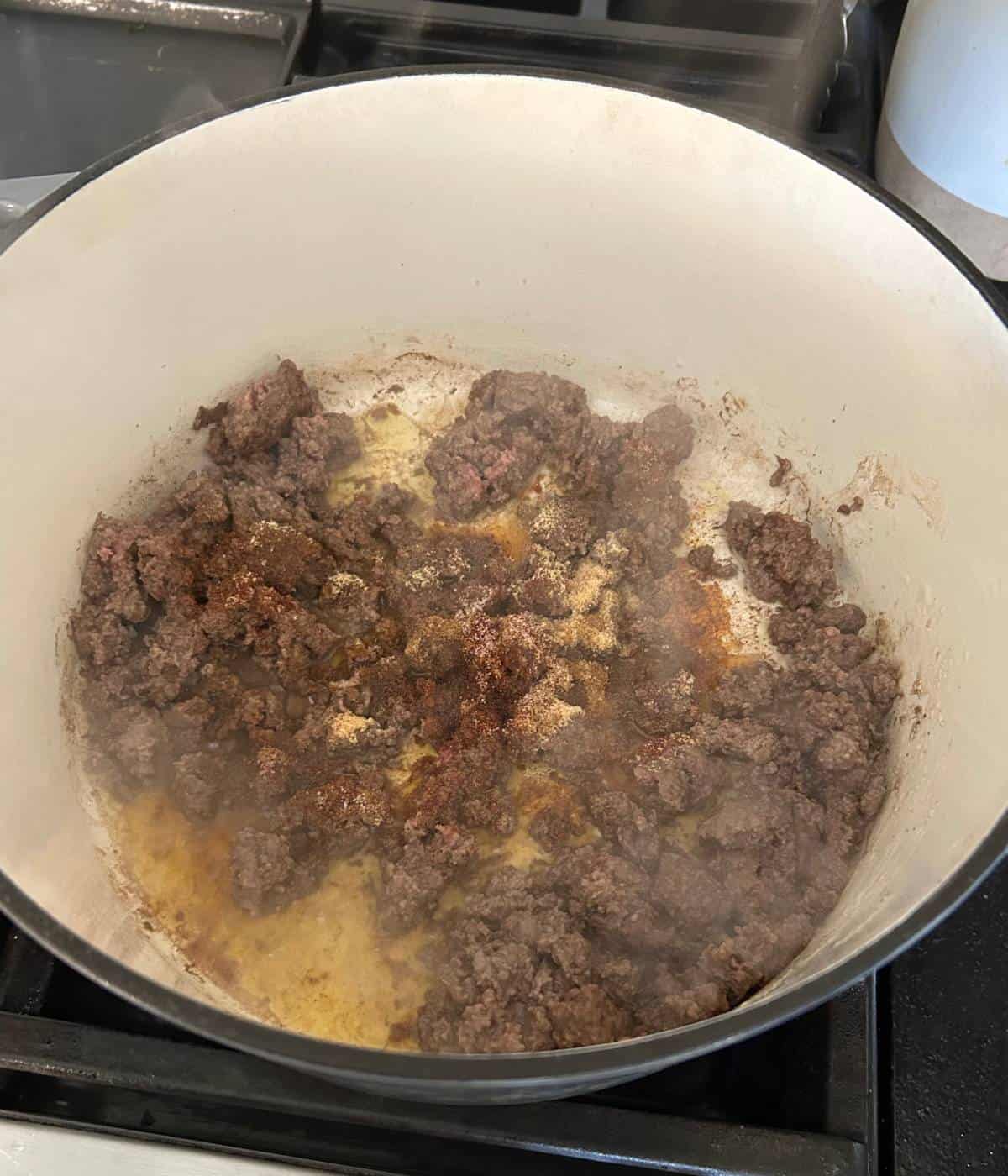 Ground beef cooking in dutch oven with seasonings.