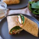Chicken wraps with spinach and honey mustard sliced in half on plate.