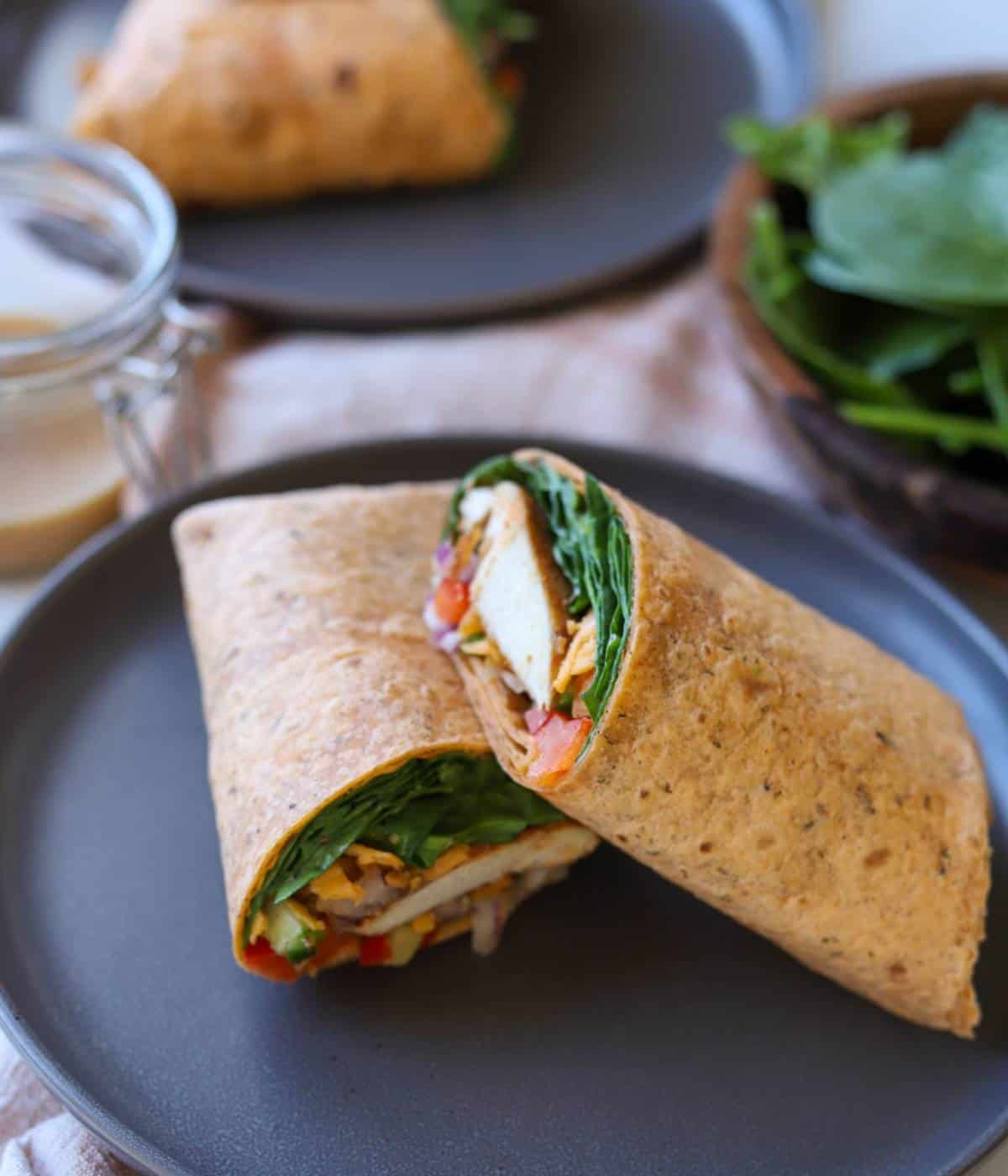 Chicken wraps with spinach and honey mustard sliced in half on plate. 