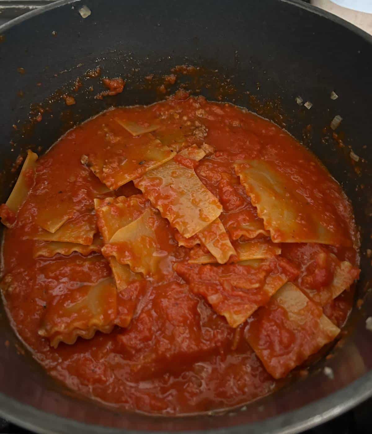 Lasagna covered in sauce in dutch oven.