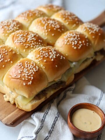 Cheeseburger sliders on wooden platter with side of sauce.