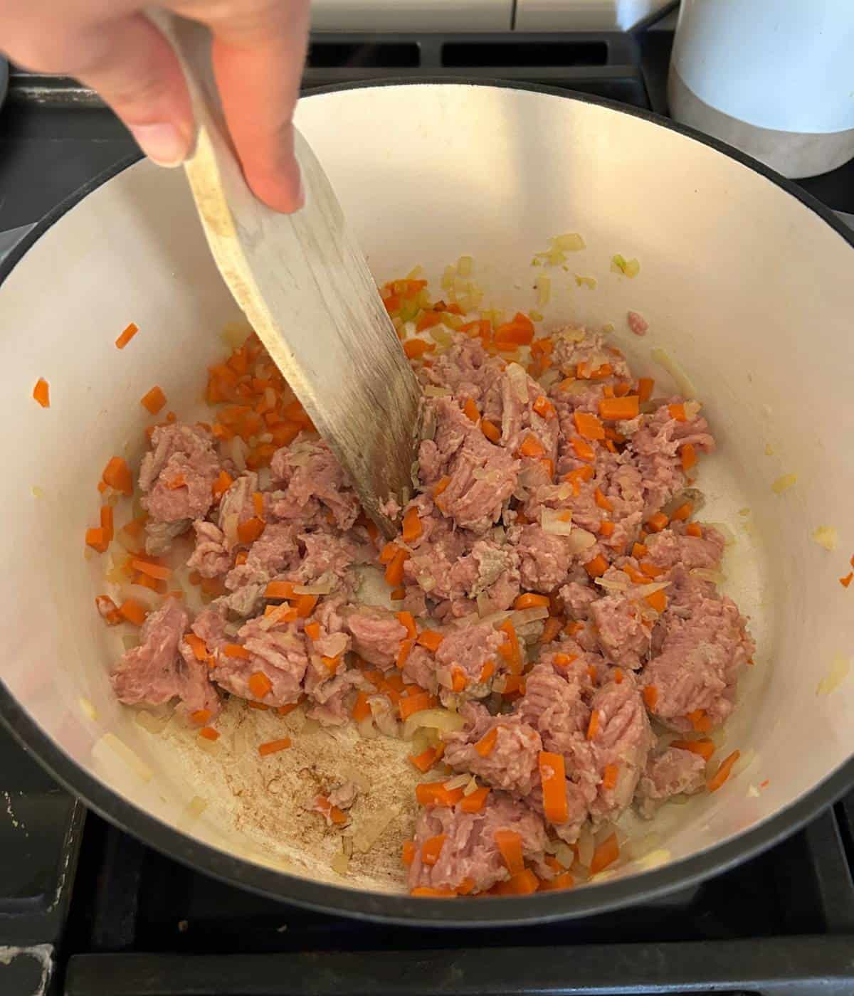 Breaking up ground turkey in pot with wooden spoon.