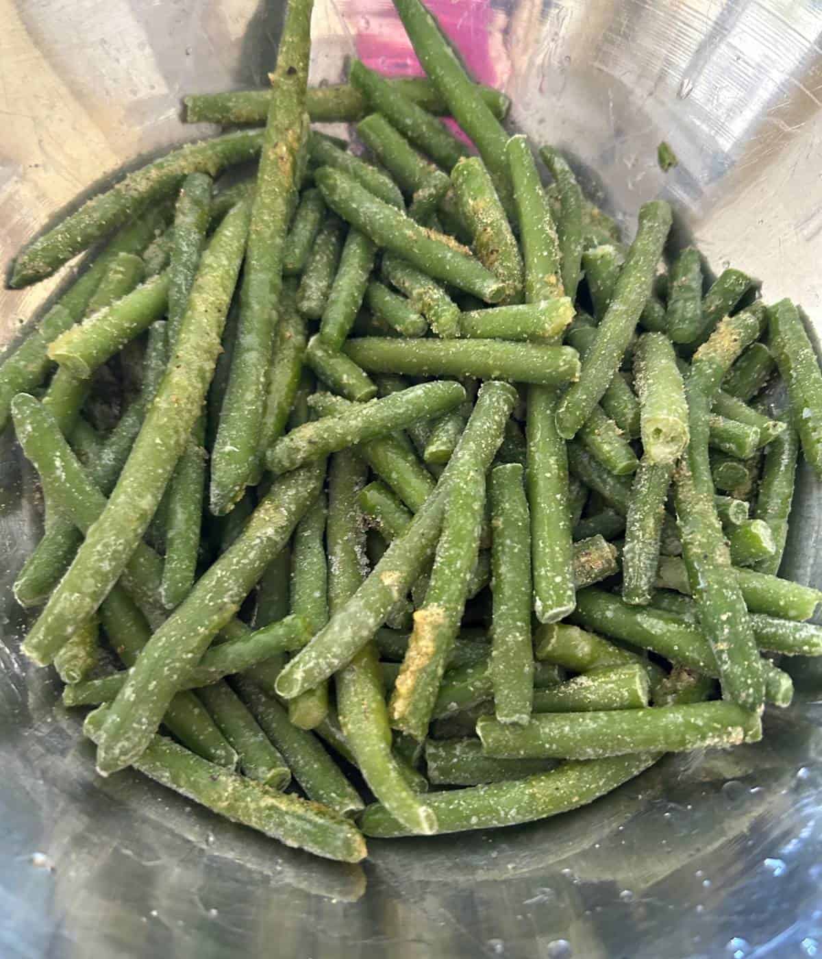 Frozen green beans tossed in seasoning in bowl.