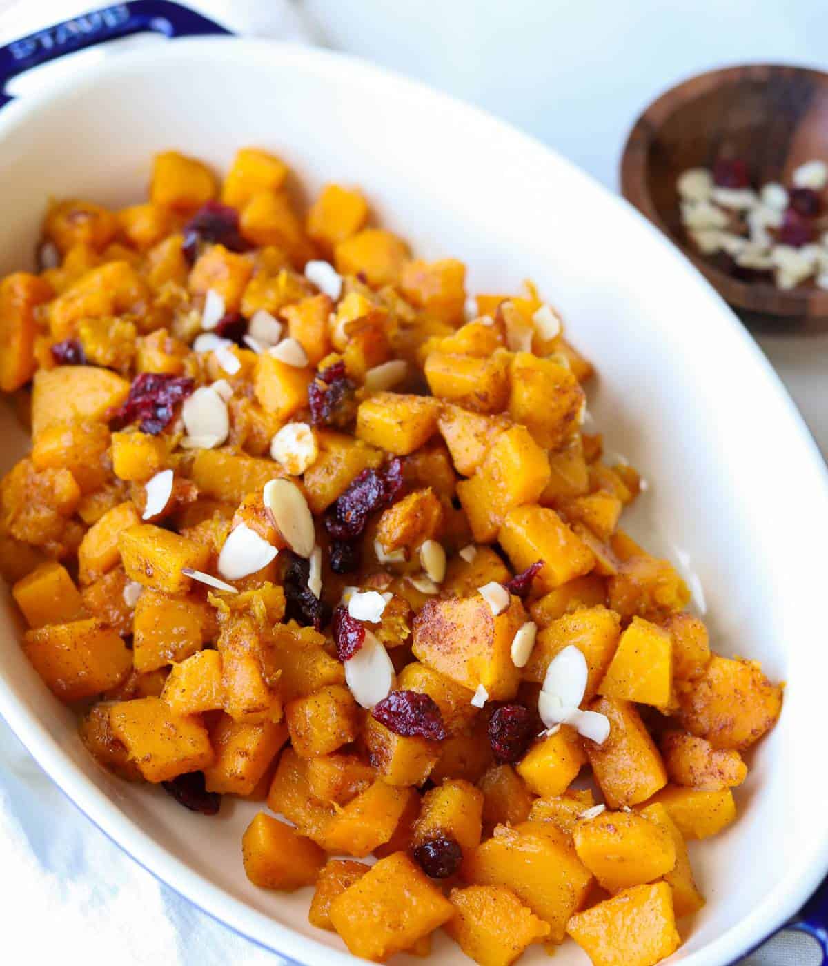 Butternut squash cubes topped with cranberry and almonds in casserole dish. 