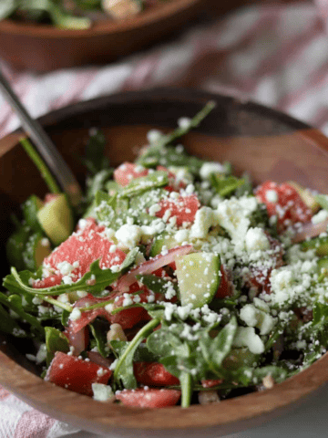 Watermelon salad with arugula and feta in wooden bowl.