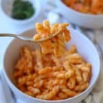 Fork holding pasta coated in carrot sauce.