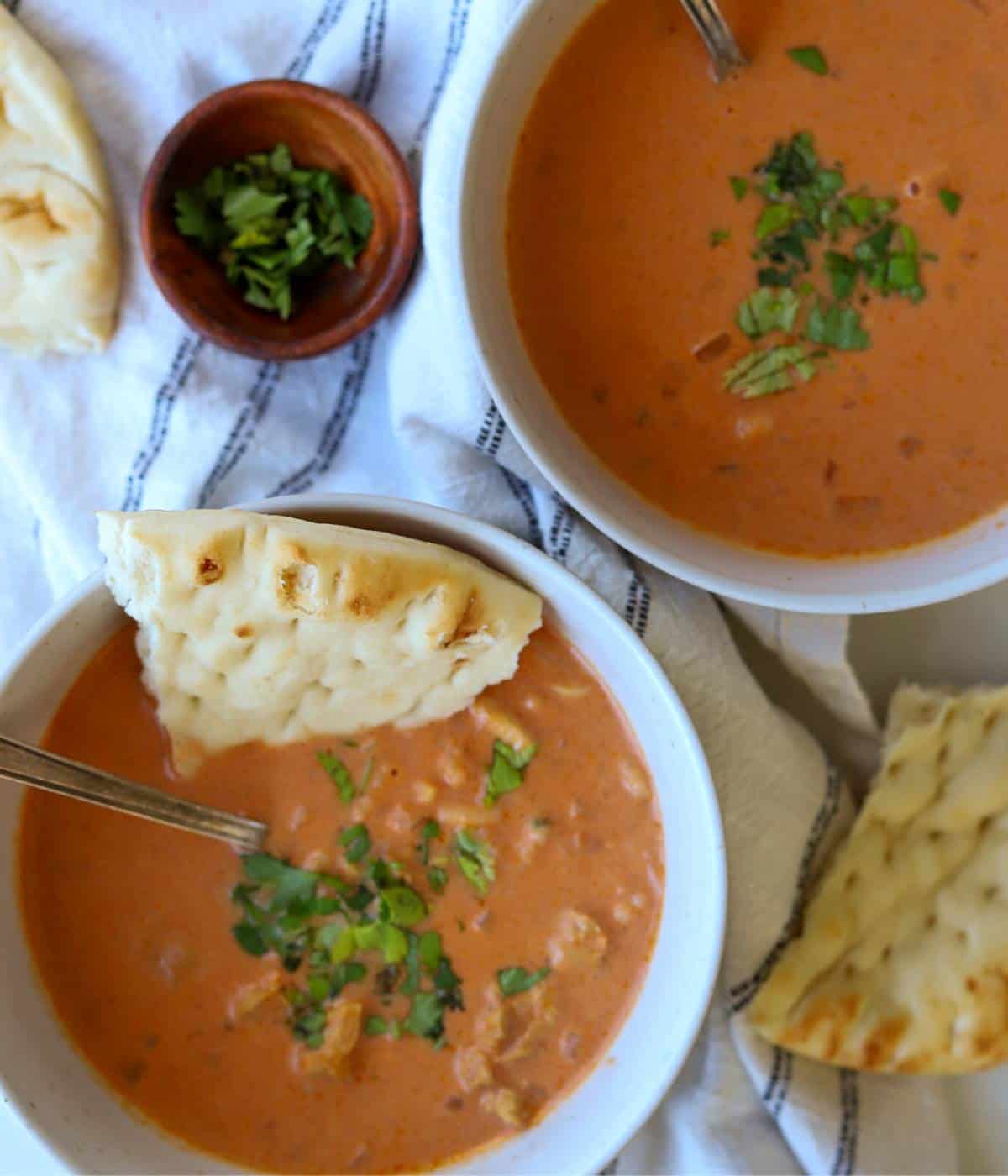 Two bowls of chicken tikka masala soup with naan bread.