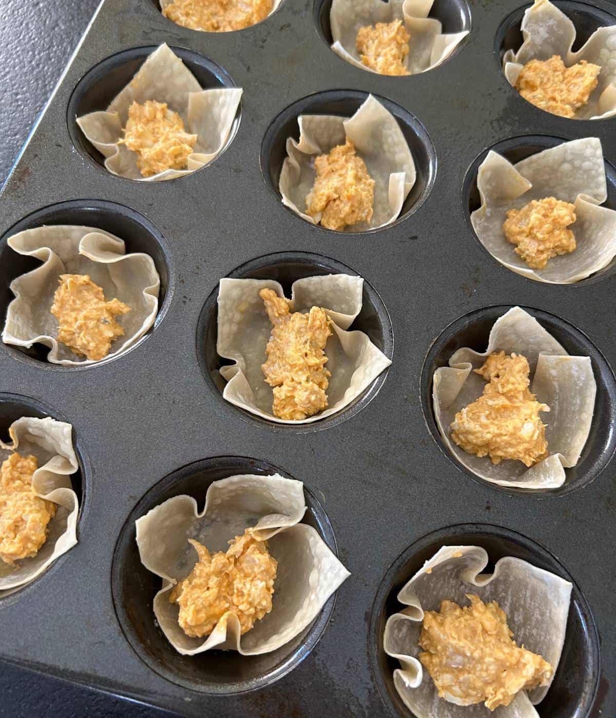 Wonton cups filled with chicken filling in muffin tin.
