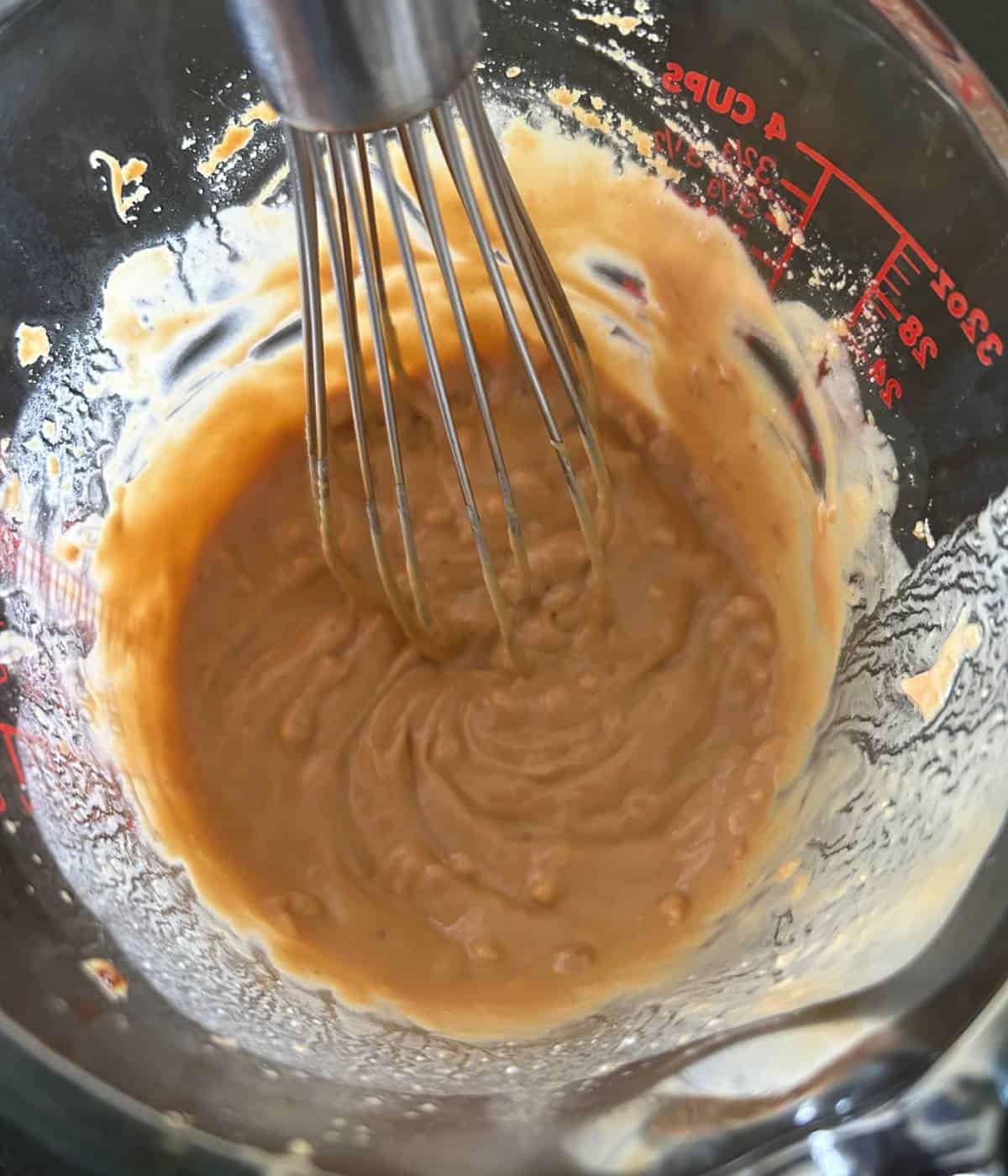 Peanut sauce in pyrex container with whisk.